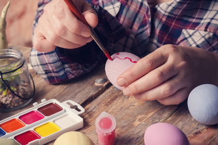 Femail hands holding paintbrush and easter egg, DIY composition on rustic wooden tableの写真素材