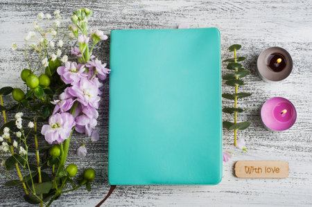 Green notepad with flowers and candles on rustic white wooden table. Still life closeup