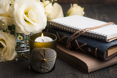 Yellow lisianthus flowers and lit candle on dark wooden background