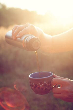 Female hand holding thermo and pouring tea in sunlight, Toned imageの写真素材