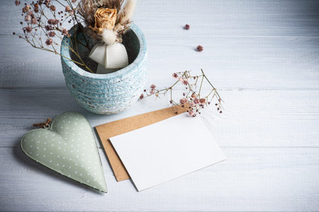 Empty blank note and kraft envelope with lit candles and green heart on white wooden table. Copy...