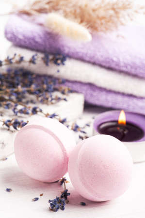 Pink aroma bath bombs in spa composition with dry lavender flowers and towels. Aromatherapy arrangement, zen still life with lit candlesの写真素材