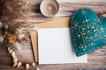 Blank note and green decorative heart, lit aroma candle and dry flowers on rustic background....