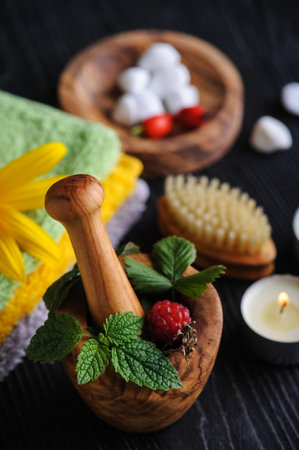 Bath balls with fresh apothecary organic aromatic herbs and berries in wooden mortar with pestle on black background. Spa with mint, peppermint, thyme leafsの写真素材