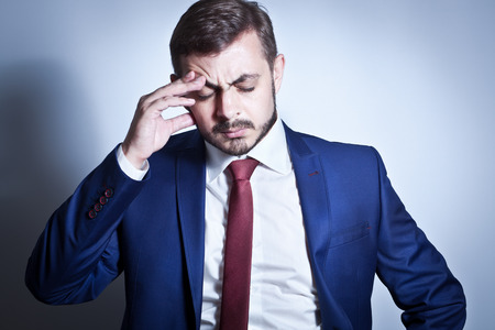 Businessman with a headache standing with his hand on his browの写真素材