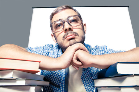 Bored young man in glasses with books looking at cameraの写真素材