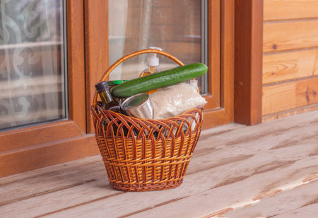 Delivery of goods to the door. Wicker willow basket with groceries and goods in front of the door of the house. Help in quarantine. Covid 19の写真素材