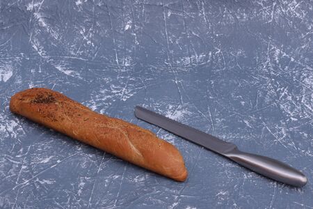 Homemade baking bread in the shape of a baguette and a knife on a gray table. Top view with copy space.の写真素材