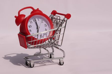 Clock in a mini shopping trolley on a white background. Shopping time concept.の写真素材
