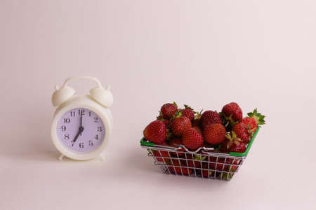 Retro clock and basket with strawberry on a white background. Harvest time concept in the garden.の写真素材