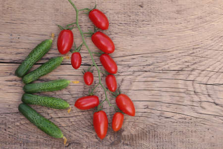 fresh cucumbers and red cherry tomatoes on vintage wooden background, top viewの写真素材