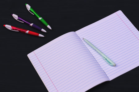 open blank notebook and multi-colored pens on a gray background. Flat lay. Copy space