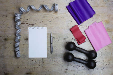 Elastic bands, tape measure, iron dumbbells and a notebook with a pen. Sports new year. The concept of sports and weight loss. Flat lay.の写真素材