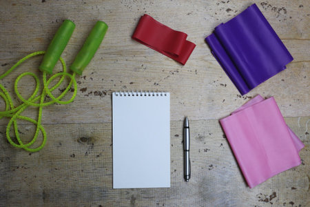 Elastic bands, skipping rope, iron dumbbells and a notebook with a pen. Sports new year. Flat lay.