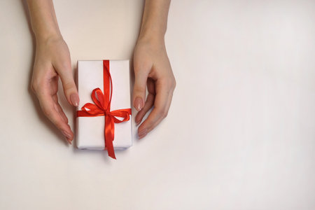 female hands with a gift box and a red ribbon on a light background. Christmas and New Year or season greeting. Selective focusの写真素材