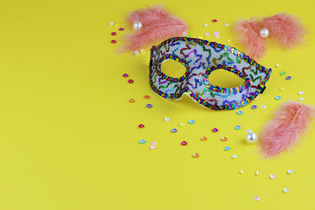 Festive background. Carnival mask with feathers on a yellow background with tinsel. Venetian. Brazilian. Copy space.の写真素材