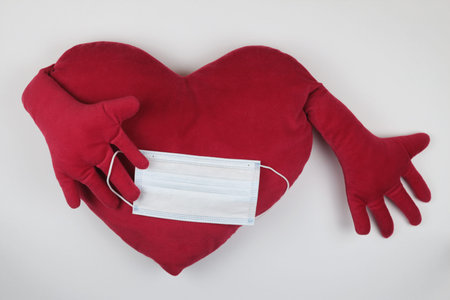 red heart shaped pillow and medical mask on a white background. Close-up