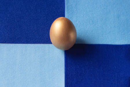 One easter egg in gold color on a classic blue background. Copy space minimal styleの写真素材
