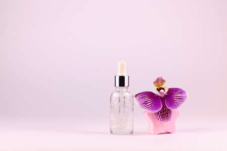 Glass cosmetic bottle with serum for skin care and orchid flower on a light background. Copy space.の写真素材