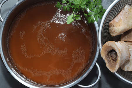 Homemade beef bone broth in a saucepan. Bones contain collagen. Close-up. View from above.の写真素材