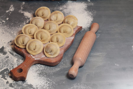 Homemade dumplings with raw meat. The Raw dumplings on a wooden board with flour and rolling pin.