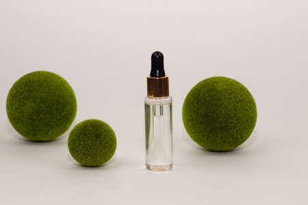 Glass bottle with a pipette. Jar with serum, transparent gel and green moss balls on a white background. Natural moisturizing serum with hyaluronic acid. Body and face care cosmetics concept.の写真素材