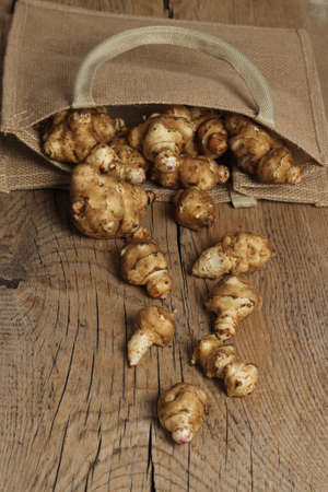 Jerusalem artichoke tubers in a burlap bag and wooden background.の写真素材