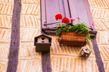 Bird house suspended from the window of an old house with wooden beams.
