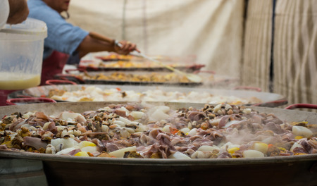 People are preparing a giant paella. Adding seafood to huge frying pans.の写真素材