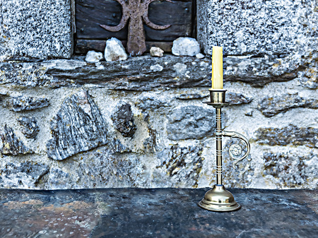 Candle on a stone table on the background of an old stone wall with a barred window.の写真素材