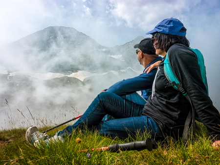 Couple man and woman sits on a hillside and admires the tops of mountains in the clouds.の写真素材
