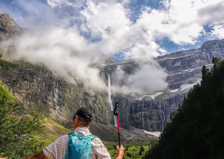 Hike in the mountains with beautiful scenery. A lone tourist admires the waterfall.の写真素材