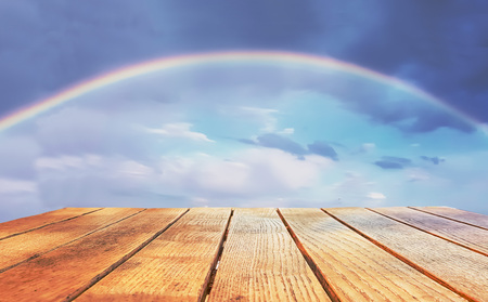 Empty surface of a wooden table on a background of a cloudy sky with a natural rainbow. Free place.の写真素材