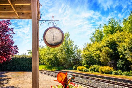 Railroad traine vintage station with a large hanging clock among flowering plants