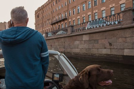 Dog owner speaking by phone and brown Labrador looking at the scenic autumn beauty from white boat