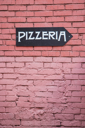 Signpost  to the pizzeria on the red brick wallの写真素材