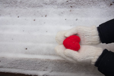 Hands in white mitterns with red heart on the snow background
