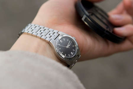 The black-silver watch on the women's hand and the lens capの写真素材