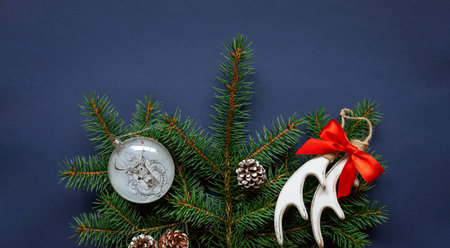 Christmas ornaments, fir tree branches, deer horns, ball, red bow on blue background.Merry Christmas and Happy Holidays greeting card.Winter xmas holiday theme.Noel, New year postcard template.Flat lay, close-up.の写真素材