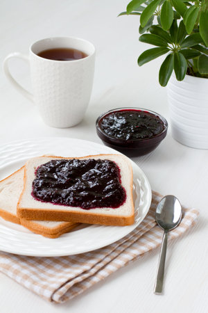 Blackcurrant jam on fresh bread and a Cup of tea. White table with a potted plant. The idea of...