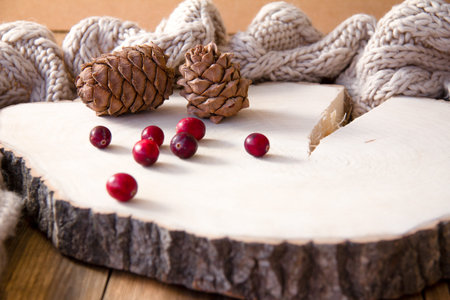 Pine cones and cranberries on a wooden stand. Knitted scarf around the perimeter. The idea of a...