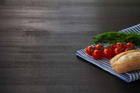 Bread roll, cherry tomatoes and dill on a napkin. Dark background. Copy spaceの写真素材