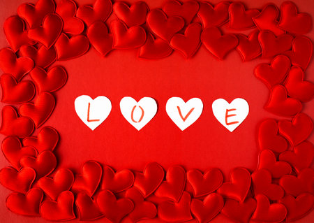 Valentine's Day greeting card. Frame of red hearts on a red background with the word Love in the center. Flat lay, top view, copy spaceの写真素材