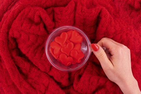 A transparent cup in the shape of a heart with red hearts is held by a woman's hand. Background of...