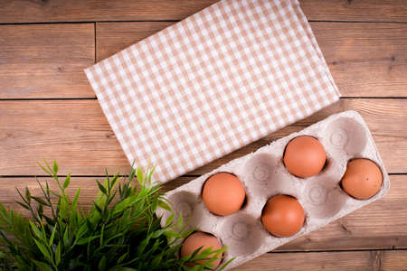 Close-up of raw chicken eggs in an egg box on a wooden background, a flower in a pot, a towel in a cage. Copy spaceの写真素材