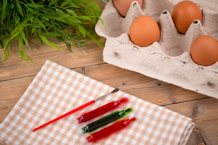 Brown eggs in a cardboard box, paint, paint brush and flowers on a wooden background. The concept of...