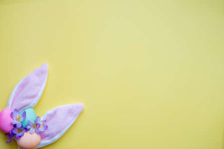 bunny ears, easter eggs and spring flowers on yellow background. simple minimalism flat lay top view copy space.の写真素材