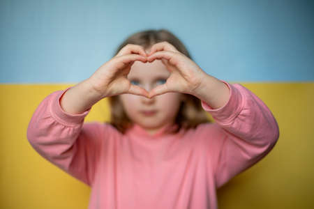 girl shows a heart with her hands on the background of the Ukrainian flag. selective focusの写真素材