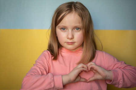 girl shows a heart with her hands on the background of the Ukrainian flag.の写真素材