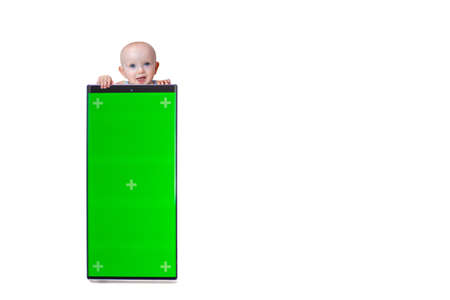 little cute baby peeking out from behind smartphone with green screen on white background isolate.の写真素材